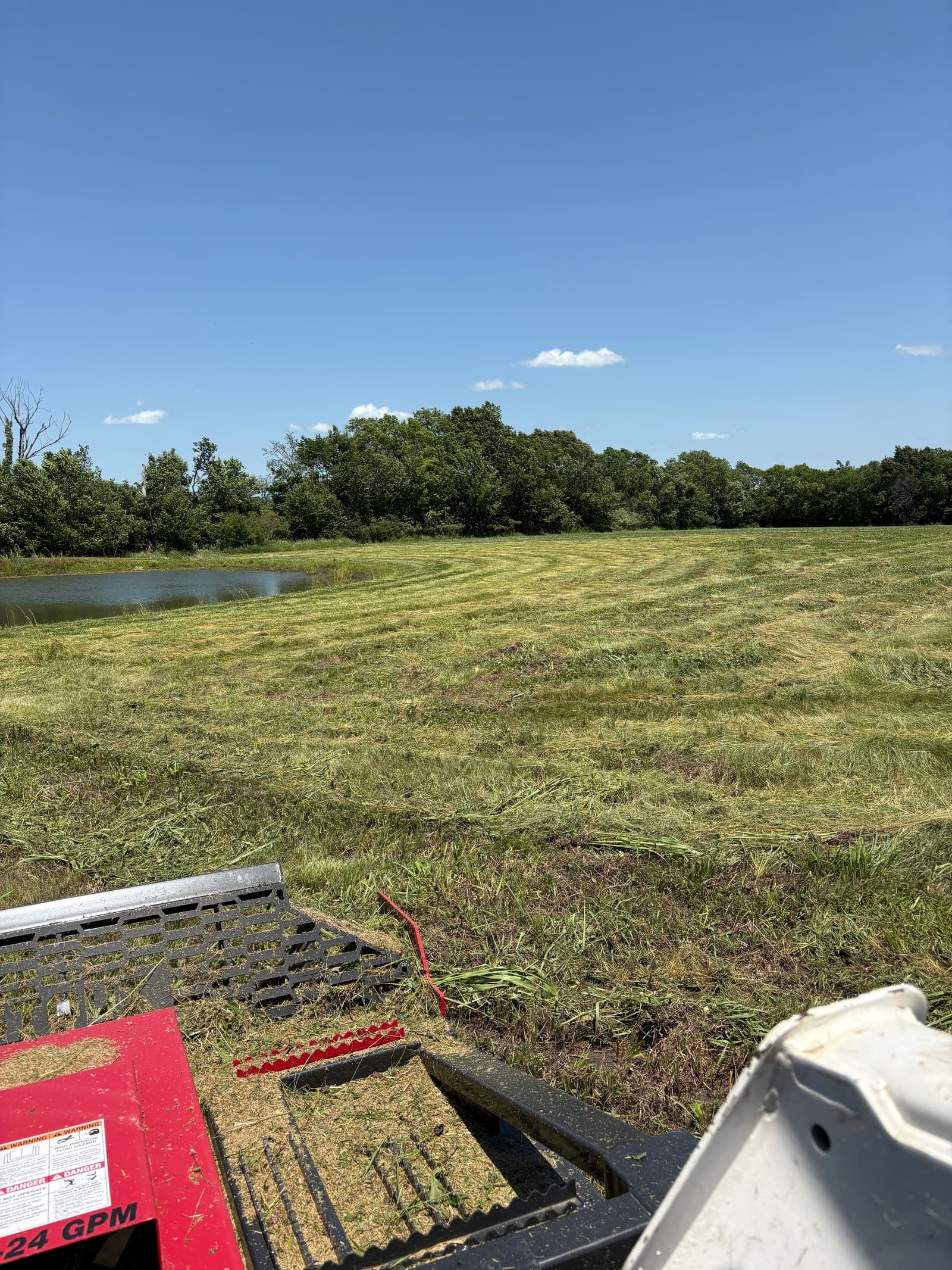 Brush hog cutter working a large field beside a pond